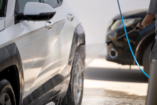 Man cleaning his vehicle, spraying water on the car body for maintenance