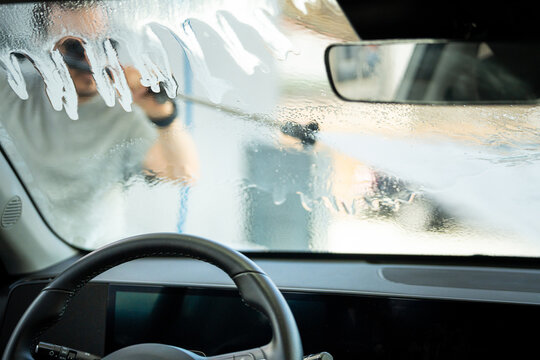 Young man washing car windshield at self-service car wash with a pressure washer