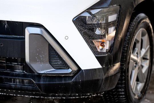 Car washing process with foam and water drops on a white vehicle headlight