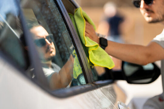 Young man drying car window after washing, a clean vehicle maintenance concept