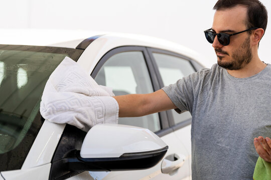 Young man drying car with a white towel at a self-service washing station
