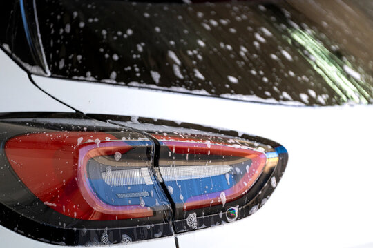 Cleaning car rear light with soap foam during pressure washing service