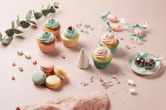 Assorted cupcakes with blue and pink frosting, macarons, and candies on a surface