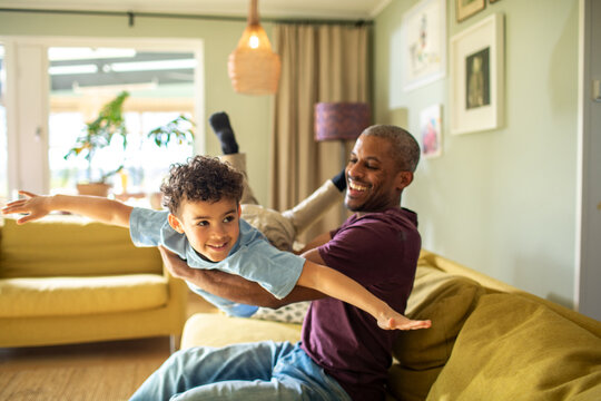Father playing airplane with son in living room