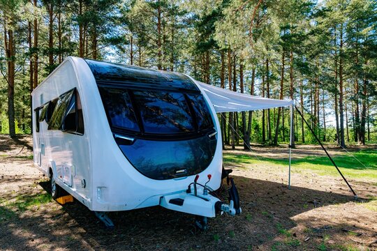 White travel trailer parked in lush green forest with extended awning and clear blue sky