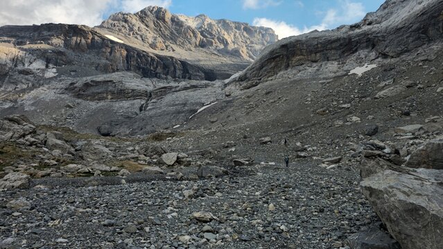Hikers trekking on rocky scree slope toward massive mountain wall in Pyrenees