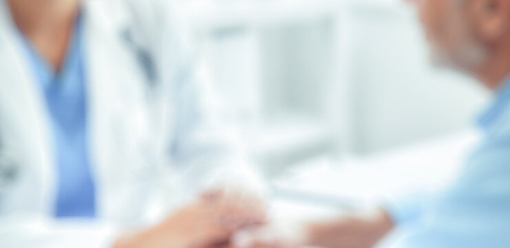 A blurred image of a healthcare professional interacting with a patient. Focus on their hands, symbolizing care and medical support in a clinical setting.