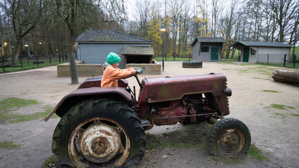 Young boy playing on vintage farm tractor outdoors © Arianne