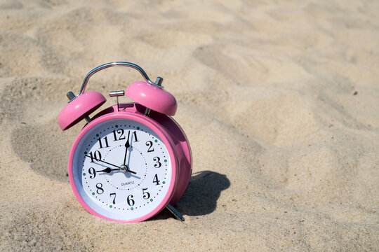 Pink retro alarm clock standing on beach sand for summer vacation countdown and time management concept