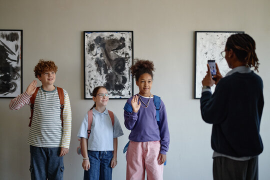 Diverse group of children posing for photo in art gallery while African American teacher taking picture with smartphone, promoting school field trips and cultural education