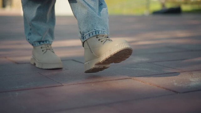 Close up of person feet in light blue jeans and beige lace up shoes walking on red brick pavement. focus remains solely on lower legs footwear details like laces texture are visible