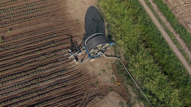 Aerial view of a reel irrigation machine positioned in a vegetable field after watering, with agricultural equipment and crop rows in Mediglia, Lombardy, Italy.