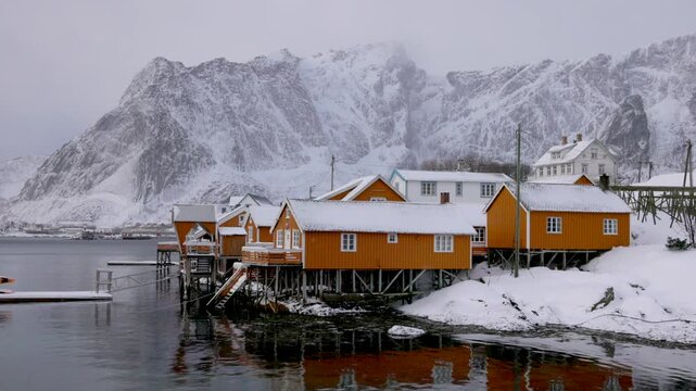 View of traditional yellow rorbuer cabins on stilts along the snowy coastline of Hamnoy, Nordland, Norway.