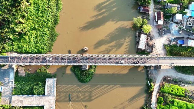 Aerial view of a steel truss bridge spanning a brown river with lush green vegetation and a small boat in Banjar Regency, South Kalimantan, Indonesia.