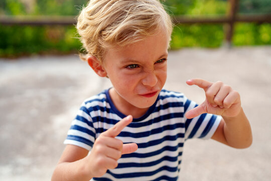 Little boy making funny face, gesturing small size with fingers, showing disapproval and unimpressed expression