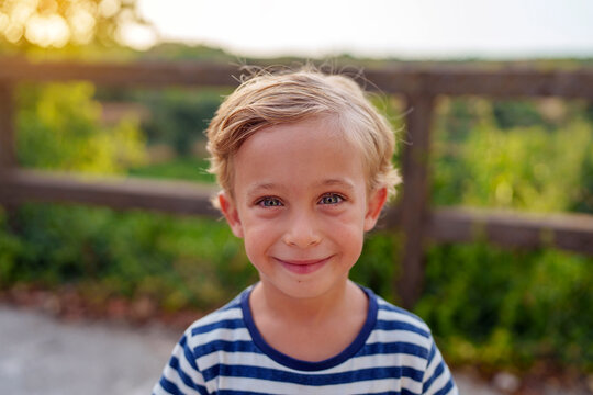 Young blonde boy smiling looking at camera, enjoying carefree childhood outdoors, genuine happy expression