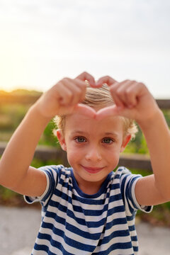 Young boy forming heart shape with hands, smiling and showing love gesture outdoors with copy space