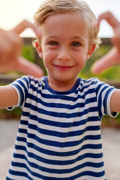 Young boy smiling, making a heart shape with his hands, conveying emotions of love, joy, and affection