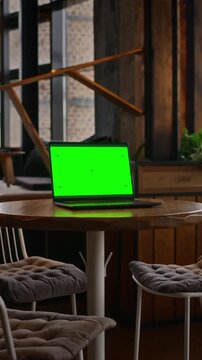 Vertical shot of laptop with chroma key green screen resting on table in coffee shop during camera pan. Perfect for remote work commercials, digital marketing and app interface replacement