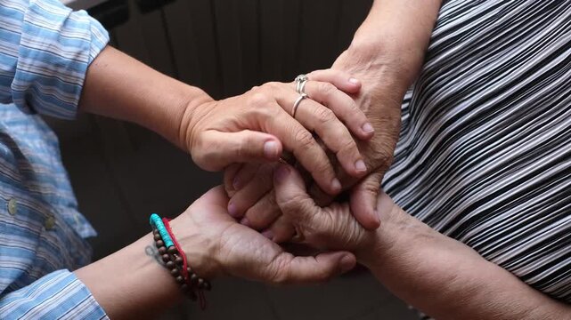 Compassionate adult daughter holding and caressing her elderly mother's wrinkled hands, showing love, care, and family support while creating a strong intergenerational bond