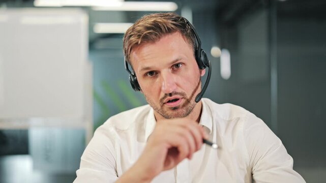 Professional wearing headset communicates via video call. Expressing points using pen, maintaining direct eye contact. Perfect for business, online support, virtual meetings, or corporate training.