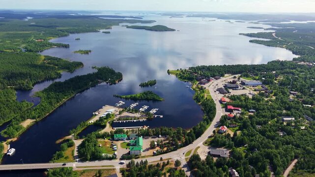 drone perspective over Juutuanjoki river winding through green pine forests into Lake Inari under scattered summer clouds in Finland