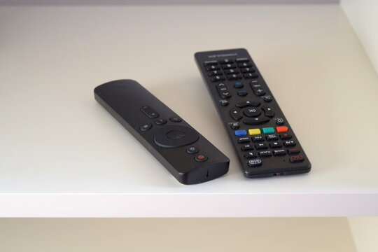 Two black TV remote controls on a white shelf of a modern media unit