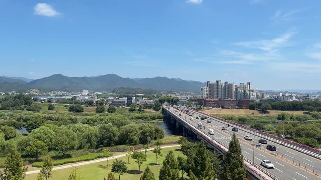High-angle aerial view of traffic flowing smoothly across a bridge over a river with lush green parks and mountain backgrounds in Daegu, South Korea 대구 북구 공항로