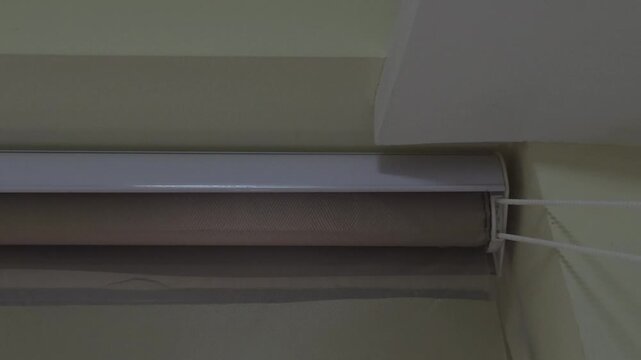 A white beaded pull chain, engaging the internal mechanism of a roller blind to lower the fabric and adjust the room's lighting