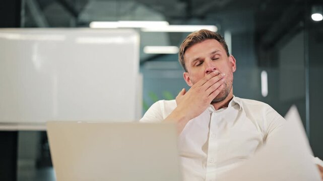 Professional experiences fatigue during work. Yawning indicates sleepiness, long hours. Concentration issues arise from prolonged tasks. Office setting shows dedication despite exhaustion.