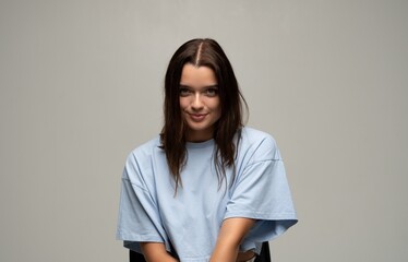 Obraz premium Brunette young woman sitting, looking at camera, having engaging expression and posing in a studio portrait