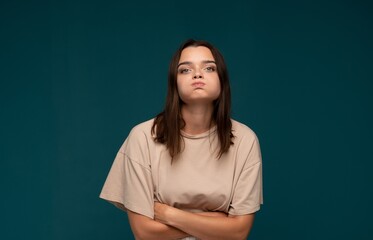 Obraz premium Young woman puffing cheeks, showing frustration and impudence, feeling annoyed and sulky with folded arms