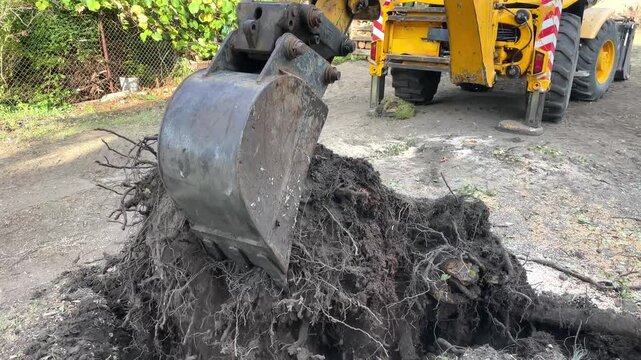 Yellow excavator arm clears broken concrete blocks and construction waste near lush green foliage, construction waste removal, site reclamation, urban redevelopment.