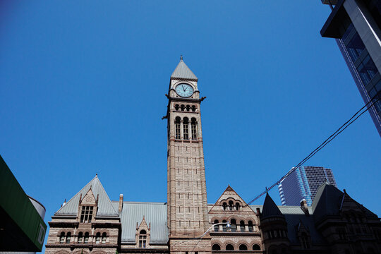 Historic Old City Hall clock tower framed by modern skyscrapers in downtown Toronto on a bright clear day. g.