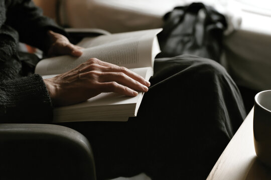 The delicate hand of a reader gently holding a book, illustrating the simple pleasures of literature and the idea of cozy afternoons spent in a thoughtfully designed living space.
