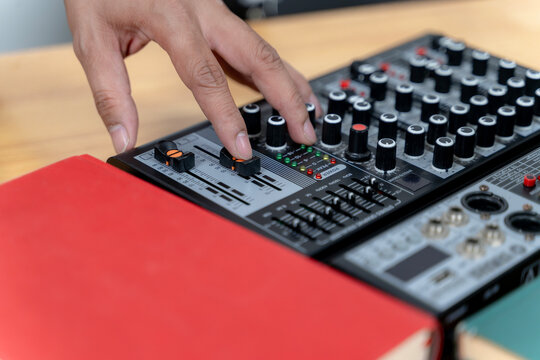 Close-up of a sound engineer's hand adjusting faders on a professional audio mixing console during a live broadcast session.
