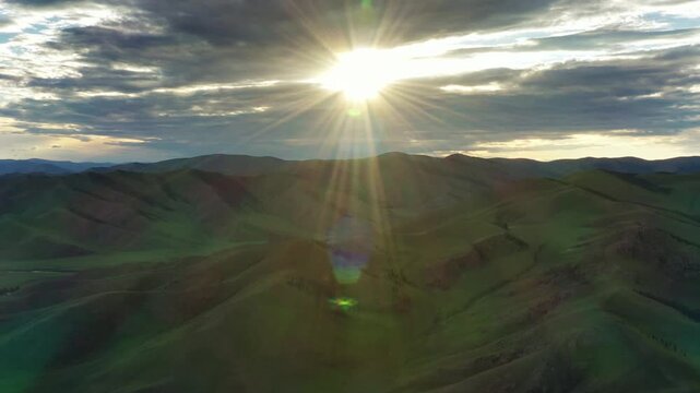 Aerial view of Orkhon Valley with rolling green hills and sun rays breaking through clouds at sunset in Xarxorin, Ovorkhangai, Mongolia.