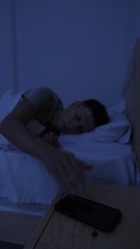Man puts smartphone away at bedtime and goes to sleep, reducing screen time for healthy sleep and digital wellbeing, vertical video