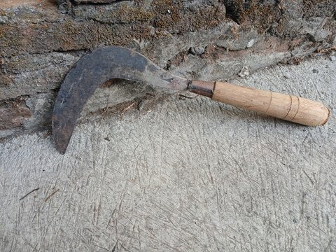 Traditional rusty sickle with wooden handle placed on concrete surface near brick wall