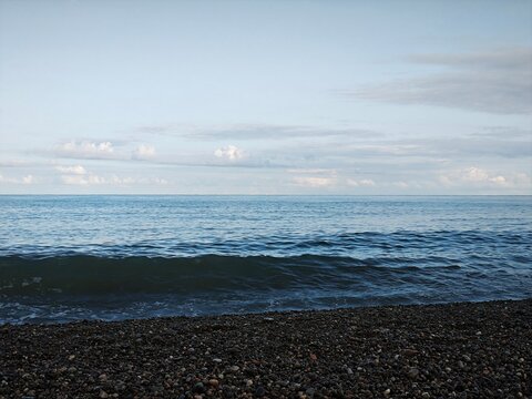 Blue sea with a rolling wave on a pebble beach. Coastal landscape under a cloudy sky