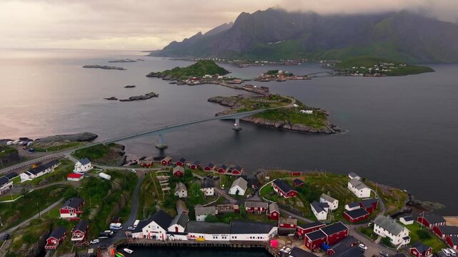 Aerial view  arched bridge of E10, asphalt road, and colorful settlement buildings along the shoreline in Hamn&oslash;y, Norway road trip travel destination 