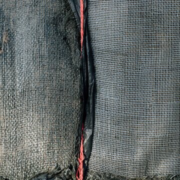 Wet woven polypropylene sandbag surface with damp textures and coral twine, featuring a heavy utilitarian feel for flood defence and disaster risk reduction