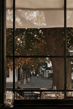 Warm autumn view through a restaurant window frames a tree-lined Parisian street, candlelit table settings, and soft evening sunlight.
