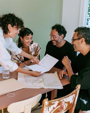 Three professionals in a relaxed job interview, reviewing a printed resume on a taupe table with soft window light for recruitment and hiring content