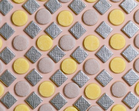 Indian sweets pattern featuring silver-leafed barfi diamonds and yellow peda discs on a blush pink background for packaging and confectionery design
