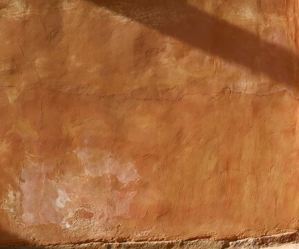 Terracotta clay orange plaster wall with a weathered chalky texture and dusty rose undertones, ideal for a warm background and copy space