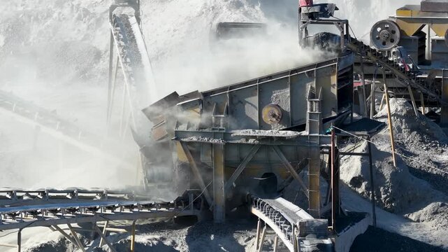 Large stone crusher machine processing rocks and generating dust at an industrial quarry site