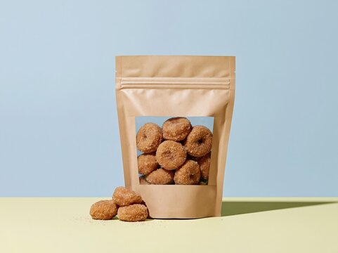 Brown stand-up pouch with mini doughnuts and a clear window, featuring a matte texture on a soft yellow surface with copy space for a mockup template