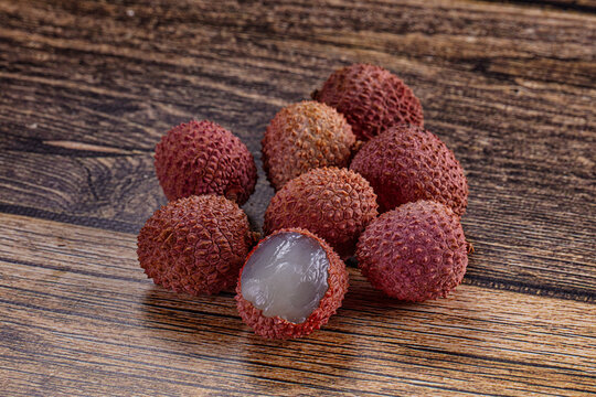 Ripe tropical lychee fruits with one peeled open on dark wooden background