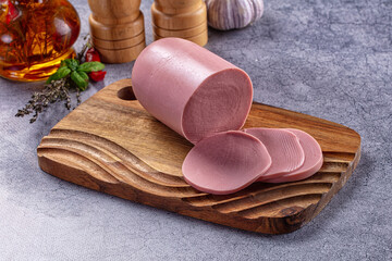 Sliced bologna sausage on wooden cutting board with fresh herbs and garlic on grey background © Andrei Starostin